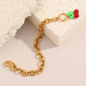 Detail of 18K gold-plated chain bracelet with red cherry pendant on white stone base