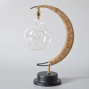 Detail of apple-shaped LED moon lamp with hemp rope and iron stand on black base