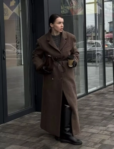 Street style shot of a woman wearing a long brown wool coat in a modern city setting
