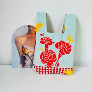 Detail of blue knitted tote bag showing red floral pattern and checkered bottom texture