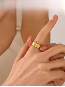 Detail of stacked gold hammer-textured wide band and beaded ring on finger