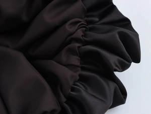 Detailed close-up showing the smooth black satin fabric and soft pleated texture of the skirt