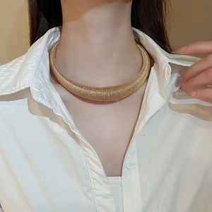 Detail of chunky gold textured choker necklace styled on a model wearing a white shirt
