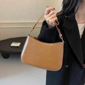 Brown smooth leather hobo shoulder bag held by a model in a minimalist setting