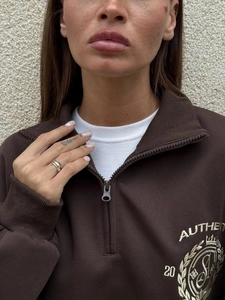 Detail view of the embroidered logo and half-zip ribbed collar on a vintage brown sweatshirt