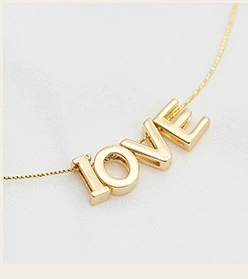 Close-up of golden LOVE letter pendant on a delicate chain over soft fabric