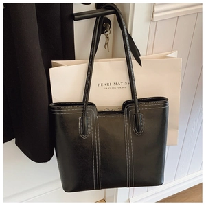 Close-up of black leather tote bag with white stitching hanging on a door handle