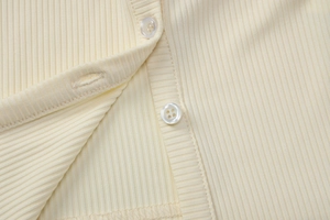 Close-up of cream ribbed knit fabric and resin buttons on a long-sleeve cardigan