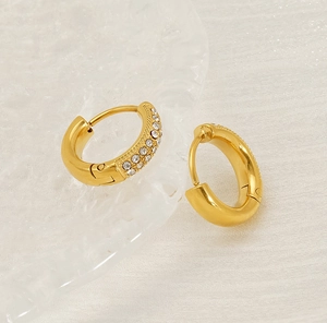 Detail of gold-plated hoop earrings with small crystals on white fabric and glass