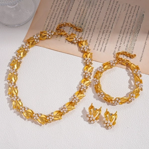 Set di gioielli dorati con motivi a foglia, perle bianche e strass su sfondo bianco