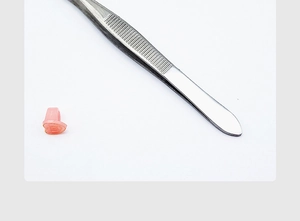 Close-up of stainless steel eyelash tweezers with small pink silicone accessory for grafting