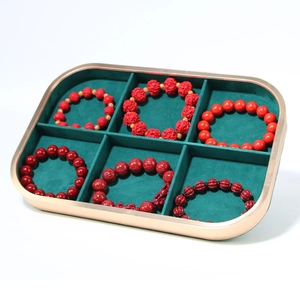 Detail of green velvet jewelry tray with gold metal frame showing red beaded bracelets