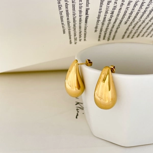Detailed view of large gold hollow teardrop earrings hanging on a white ceramic mug edge