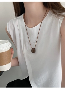 Brown irregular oval pendant with dark brown cord necklace worn by a model in casual style