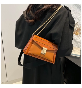 Detail of orange crocodile pattern bag with gold chain strap worn by a model