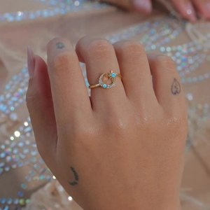 Detailed view of gold star and moon ring with opal inlay on finger with bokeh background