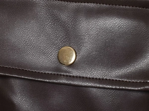 Détail de la texture cuir marron foncé avec bouton doré et coutures précises