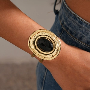 Macro detail of wide golden cuff bracelet with hammered texture and oval black gemstone