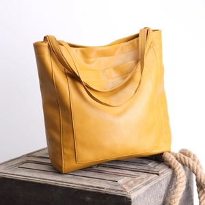 Détail du sac cabas vintage en cuir ciré jaune gingembre sur un coffre en bois