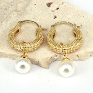 Detail of gold textured hoop earrings with dangling white pearls on stone background