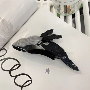 Detailed view of a whale-shaped hair claw clip in grey acetate on an open book