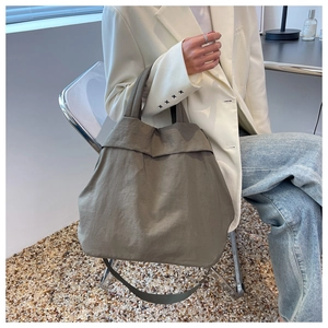 Detailed view of the large grey-green nylon tote bag worn by a model in a modern room