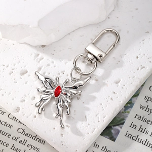 Close-up of a silver butterfly keychain with a red gemstone on a textured surface