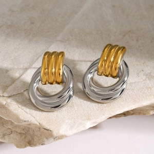 Detail of interlocking silver rings and gold striped stud earrings on beige stone