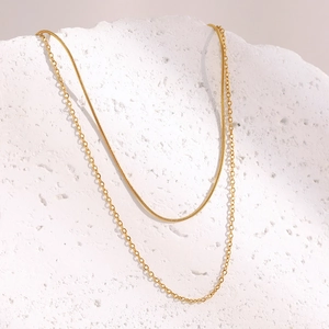 Detailed view of layered 18K gold plated snake and cable chain necklace on textured stone