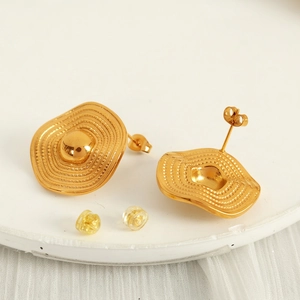French style gold wavy disk earrings with textured circular pattern on stone stand