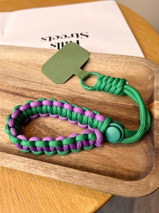 Detail of green and purple braided wrist lanyard with metal clip on a wooden tray