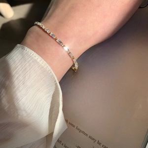 Detailed shot of a gold tennis bracelet with rectangular AAA zircons on a woman's wrist