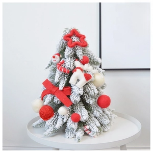 Miniature snow-flocked Christmas tree with red and white festive knit ornaments on a table