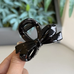 Close-up of black glossy bow-shaped hair claw clip held in hand for size comparison