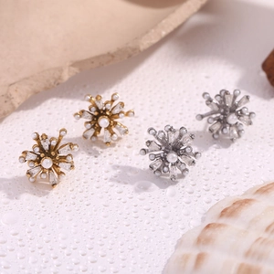 Close-up of gold and silver snowflake stud earrings with pearls and zircons on white stone
