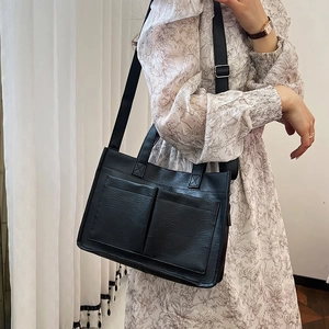 Minimalist black faux leather tote bag with dual front pockets worn by a model in soft light