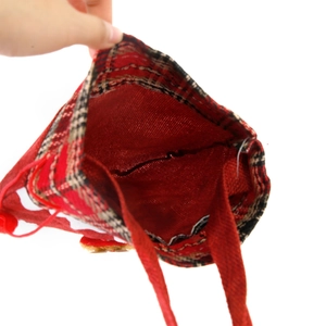 Sac cadeau de Noël rouge avec bordure à carreaux, tenu en main pour montrer le volume