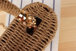 Detailed close-up of woven straw handbag handle with gold metallic ring hardware
