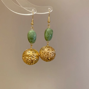 Vue macro de boucles d'oreilles chinoises en résine avec billes dorées évidées et perles vertes