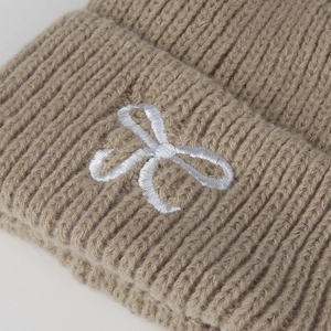 Gros plan du bonnet en tricot camel épais avec broderie de nœud blanc détaillée