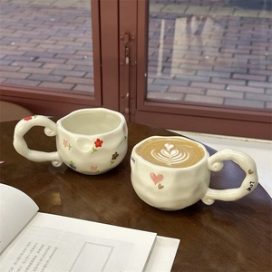 Close-up of irregular handmade ceramic coffee mug with hand-painted floral heart pattern