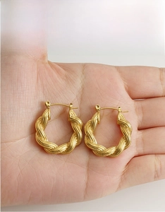 Detail of gold twisted hoop earrings with textured finish held in hand for size view