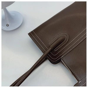 Close-up of dark brown leather tote featuring white contrast stitching and metal zipper