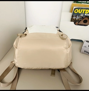Detail view of the reinforced bottom and padded straps on this beige nylon backpack