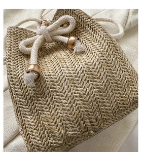 Close-up of woven straw bucket bag with drawstring closure and golden metal accents