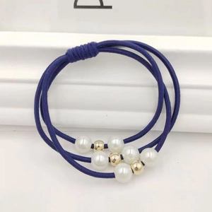 Détail d'un élastique à cheveux bleu marine avec perles blanches et dorées sur fond blanc