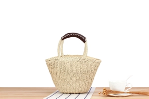 Close-up of woven straw tote bag with brown leather handle and white stitching detail