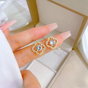 Luxurious gold clover stud earrings with sparkling crystals held between fingers