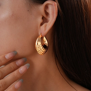 Close-up of a gold geometric textured hoop earring worn by a model on the ear
