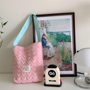 Pink heart-quilted tote bag with light blue straps shown in a cozy home setting